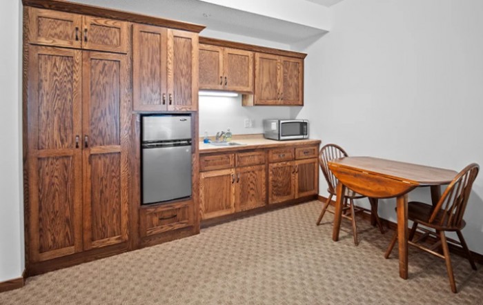 A small kitchen area with wooden cabinets, a mini fridge, microwave, and a dining table.