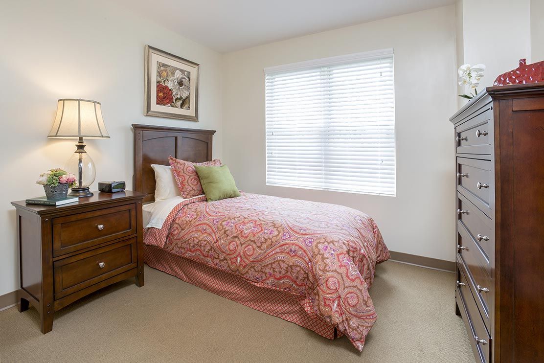 A cozy bedroom with a single bed, wooden furniture, and a window letting in natural light.
