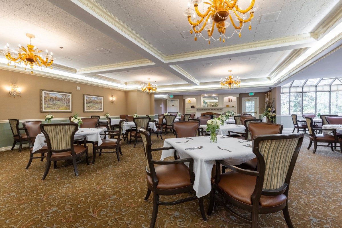 An elegant dining room with neatly arranged tables and chairs, adorned with chandeliers.