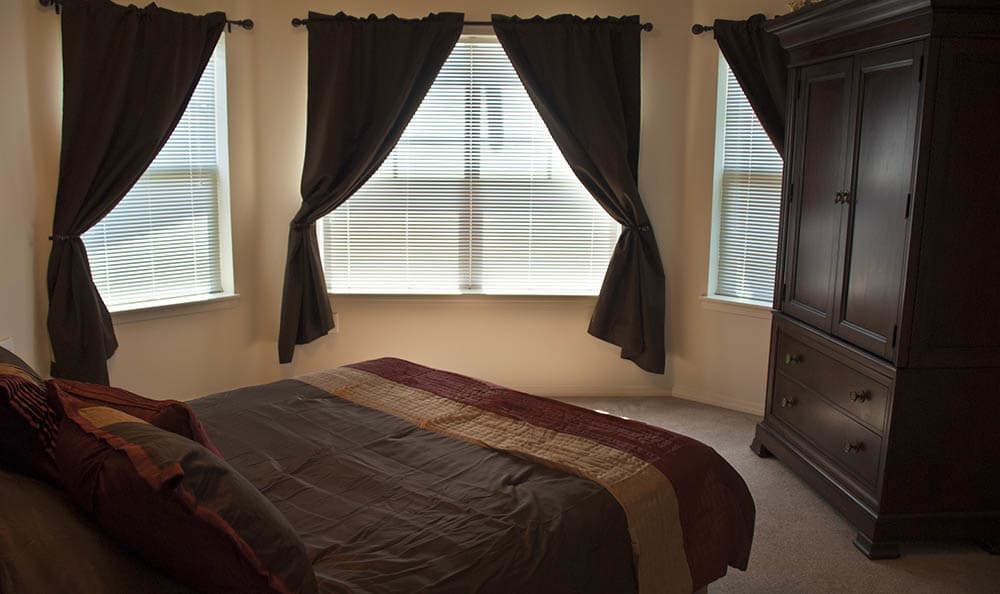 A cozy bedroom with a neatly made bed and dark curtains framing the windows.