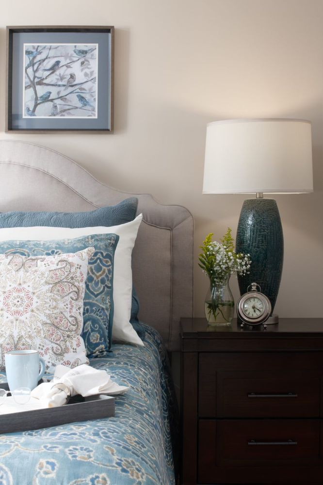 A cozy bedroom setup with a bedside table featuring a lamp, clock, and decorative pillows.
