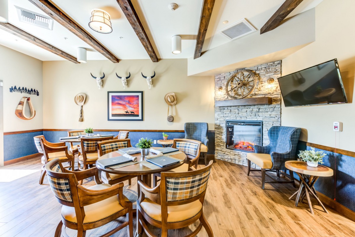 A cozy restaurant dining area with wooden tables and chairs, decorated with a stone fireplace and wall art.