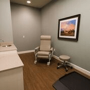 A tidy and minimalistic medical examination room with a chair, stool, and wall art.
