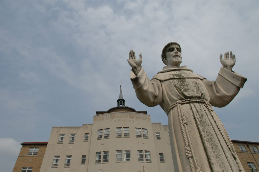 A statue of a religious figure stands prominently in front of a building against a cloudy sky.