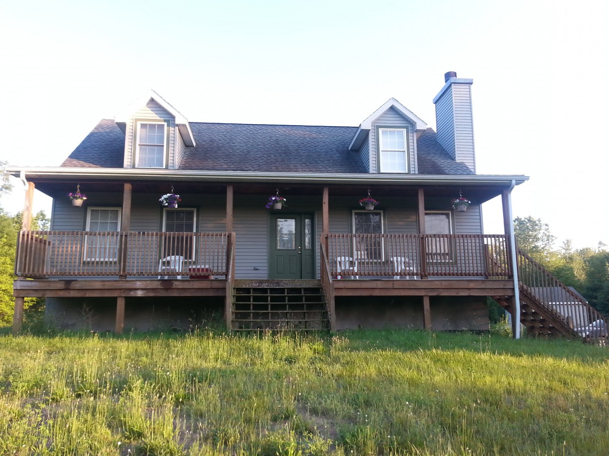 A country-style house with a spacious porch and grassy front yard.