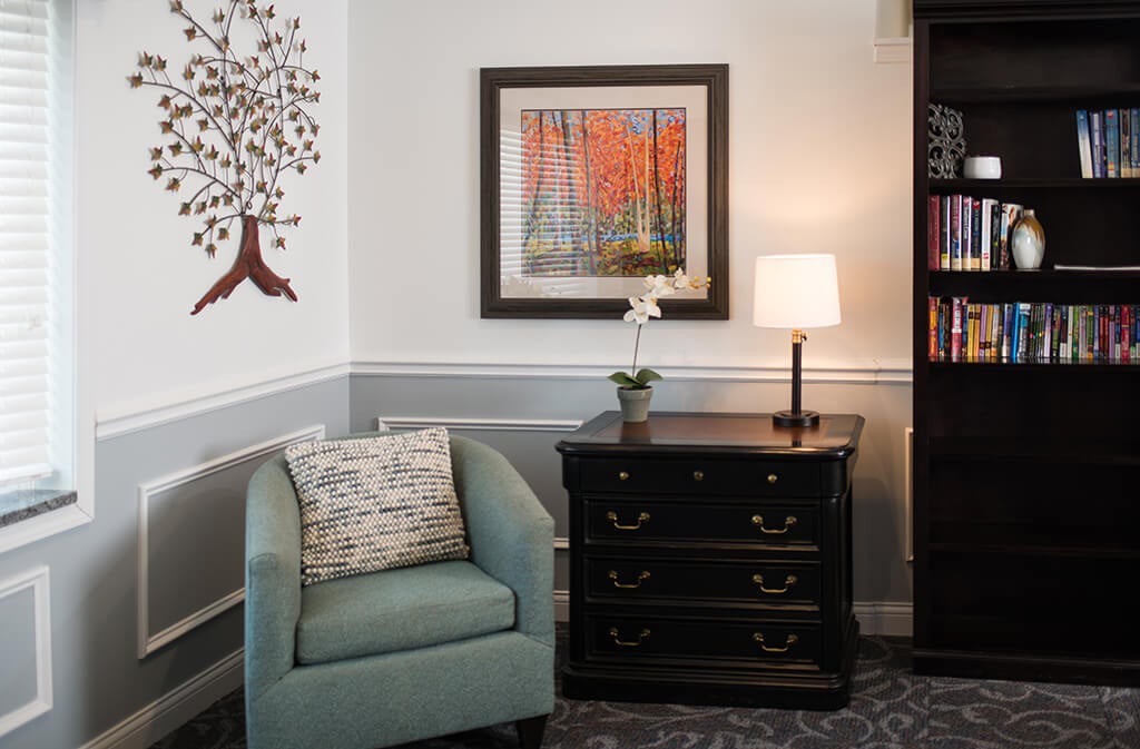 A cozy living room corner featuring an armchair, a small table with a lamp, and colorful artwork on the wall.