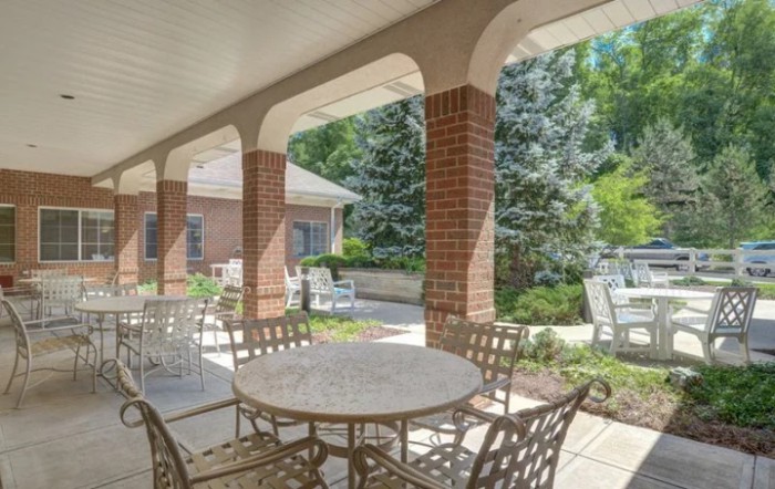 A covered patio with tables and chairs overlooking a garden.