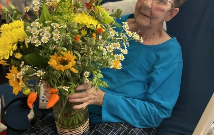 An elderly person holding a colorful bouquet of flowers indoors.