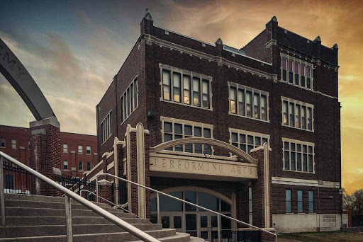 A historic brick building with large windows and a decorative entrance, set against a dramatic sky.