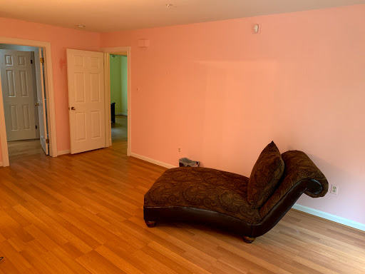A cozy living room featuring a chaise lounge, soft pink walls, and warm wooden flooring.