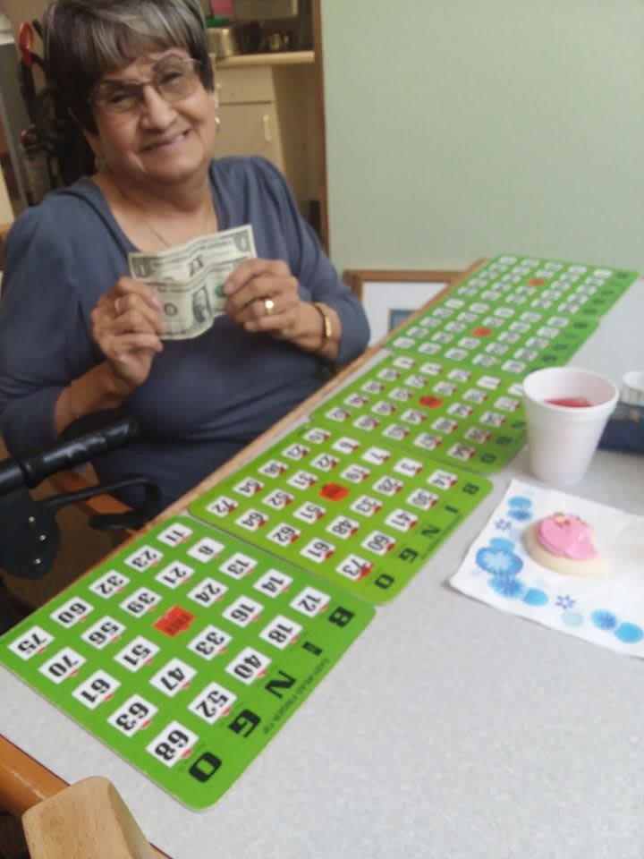 An elderly woman happily holding money after winning a bingo game.