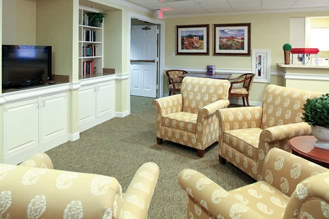 A cozy living room with patterned armchairs and framed paintings on the wall.