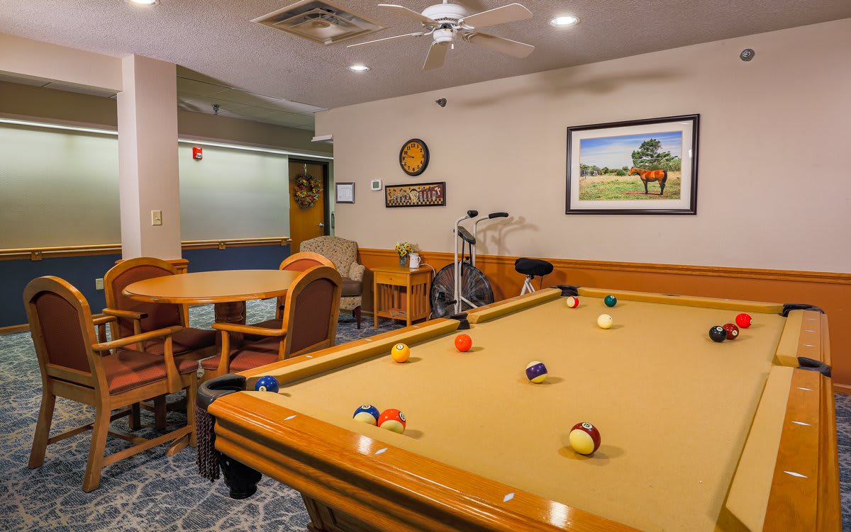 A cozy game room featuring a billiards table with pool balls, surrounded by chairs and tables.