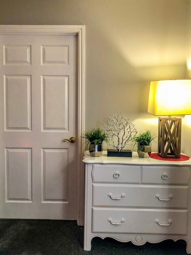 A cozy bedroom corner with a white dresser and a warm lamp.