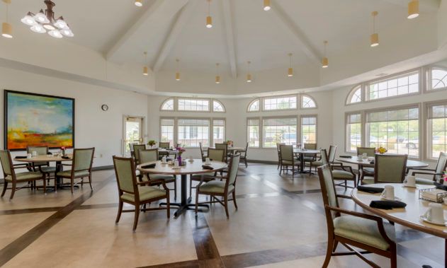A spacious dining room with multiple tables and chairs, featuring large windows and modern lighting.
