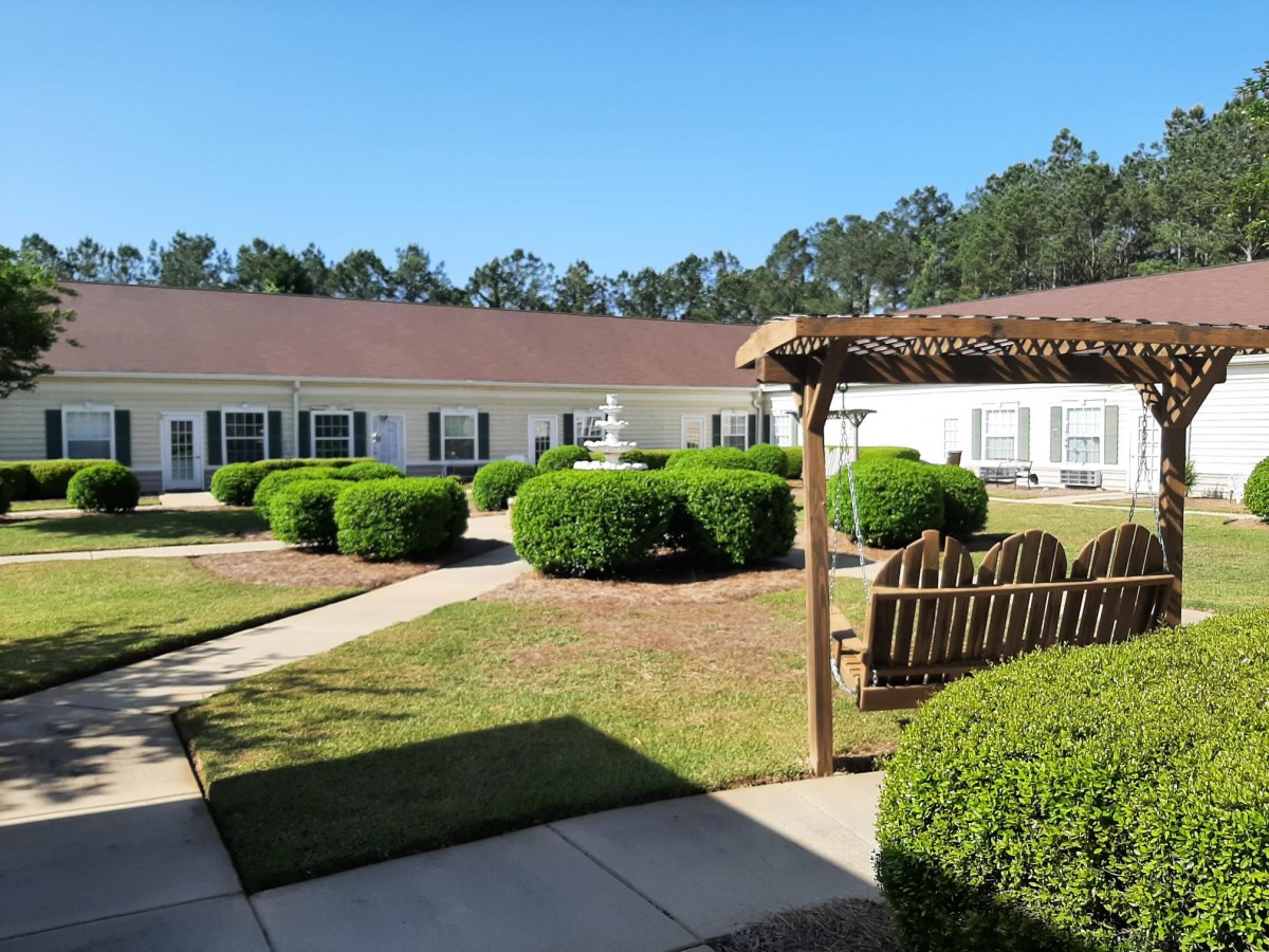 A well-manicured courtyard with a pergola and neatly trimmed bushes against a clear blue sky.