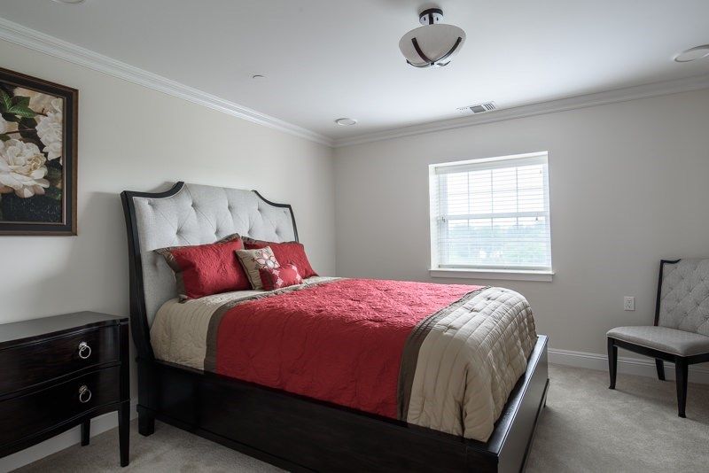 A neatly arranged bedroom with red and beige bedding, featuring a large window that allows natural light to brighten the room.