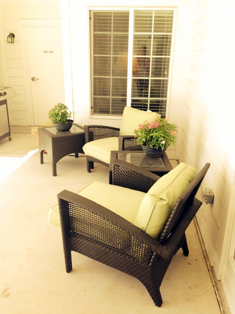 A cozy patio setting with cushioned chairs, a table, and decorative plants.