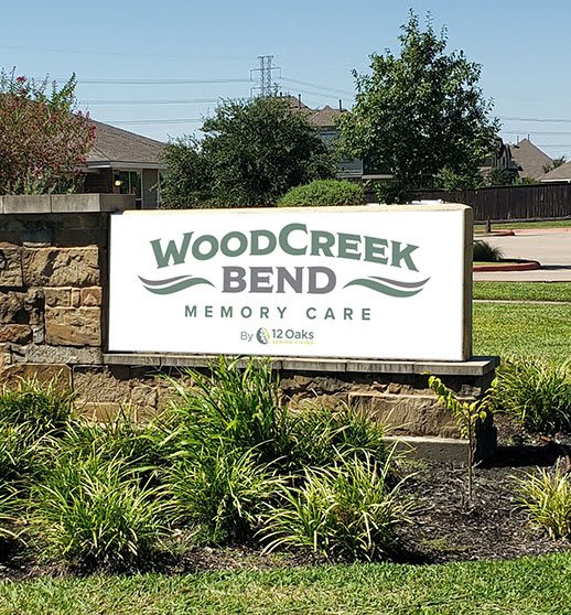 Sign for WoodCreek Bend Memory Care surrounded by landscaping.