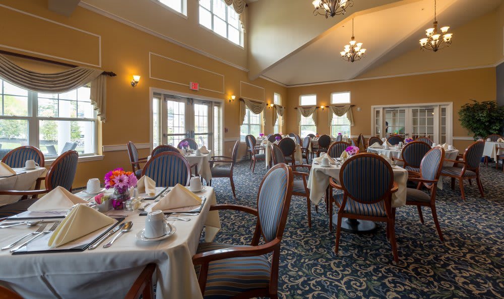 An elegant dining room setup with neatly arranged tables and chairs, adorned with flowers.