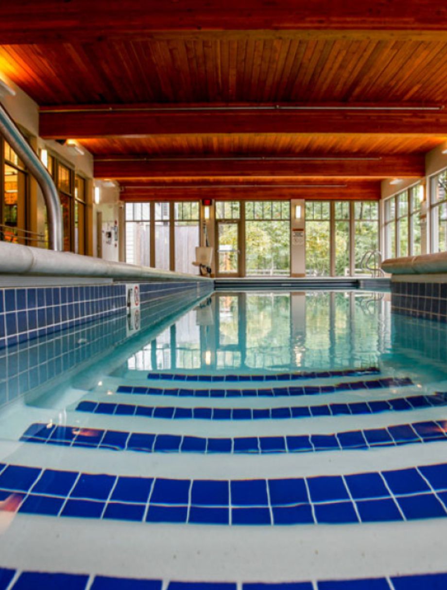 A serene indoor swimming pool with blue-tiled steps and large windows allowing natural light to illuminate the space.