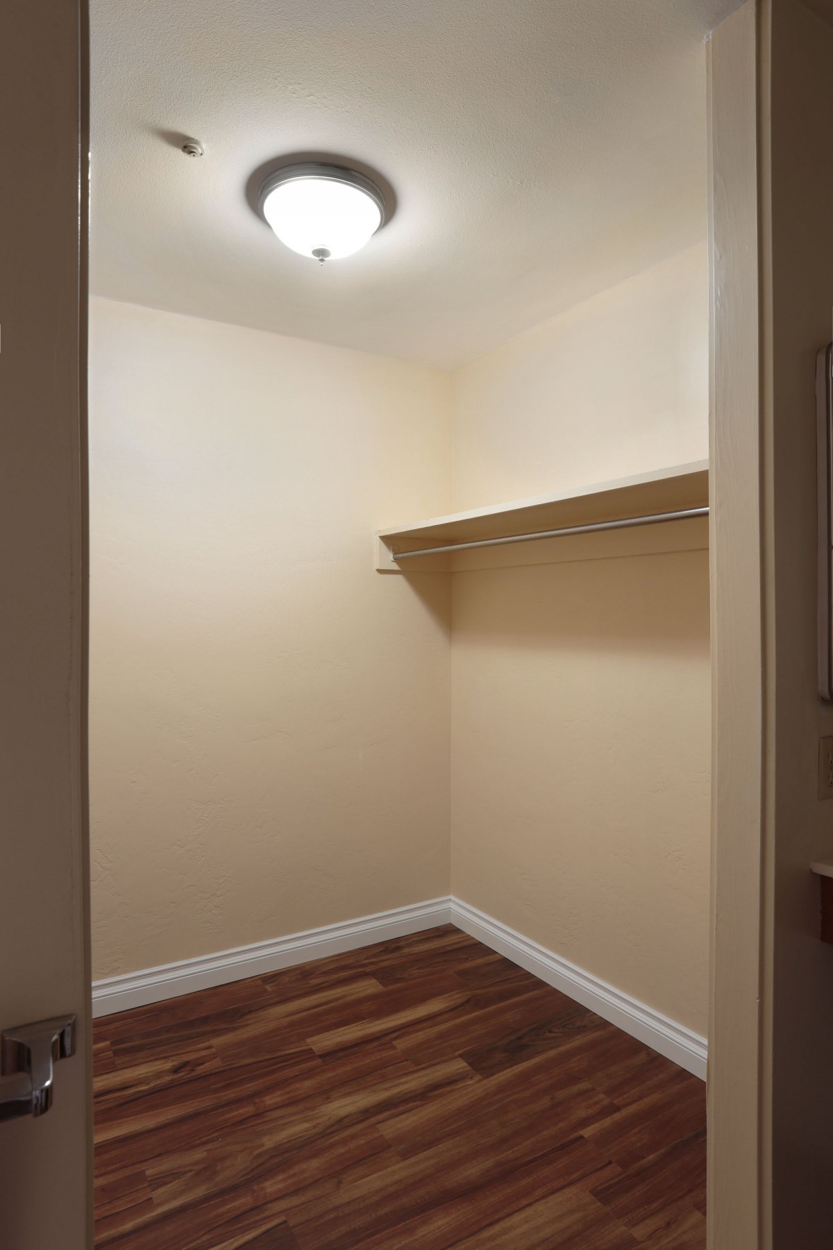An empty walk-in closet with wooden flooring and a single shelf.