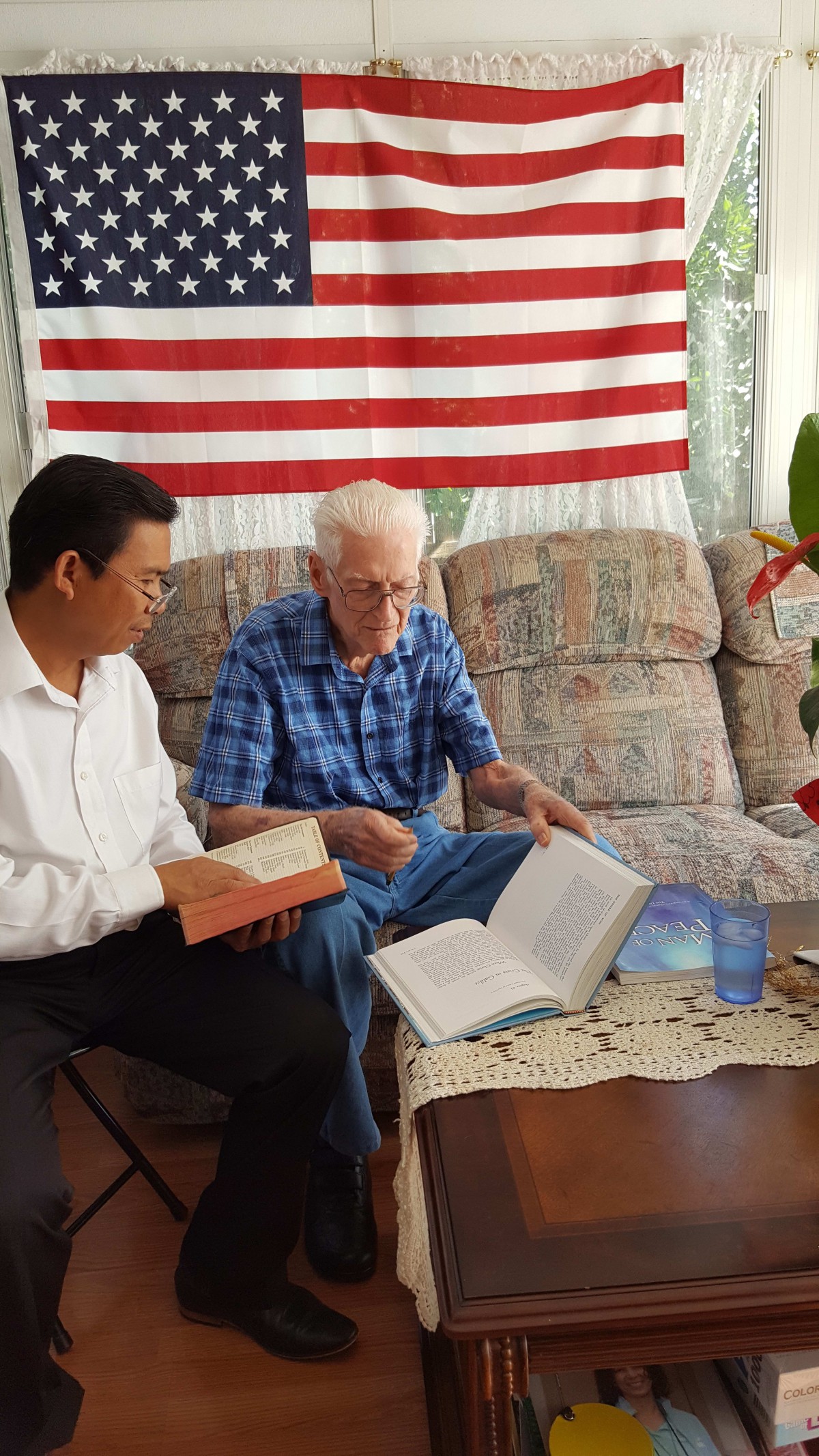 Two men sitting on a couch having a discussion while reading books.