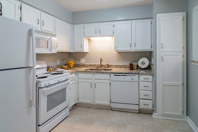 A modern kitchen with white cabinets, a stove, sink, and dishwasher.