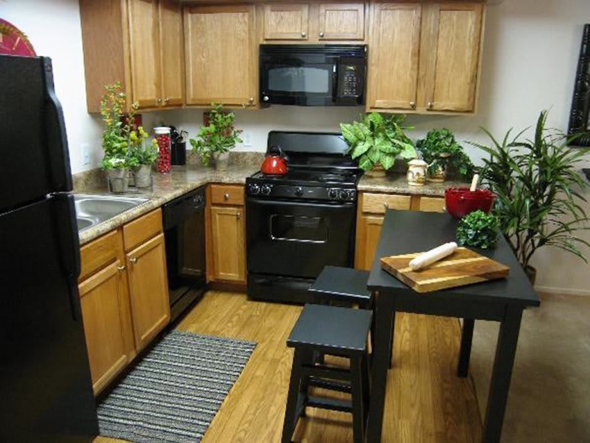 A cozy kitchen with wooden cabinets, black appliances, and greenery.