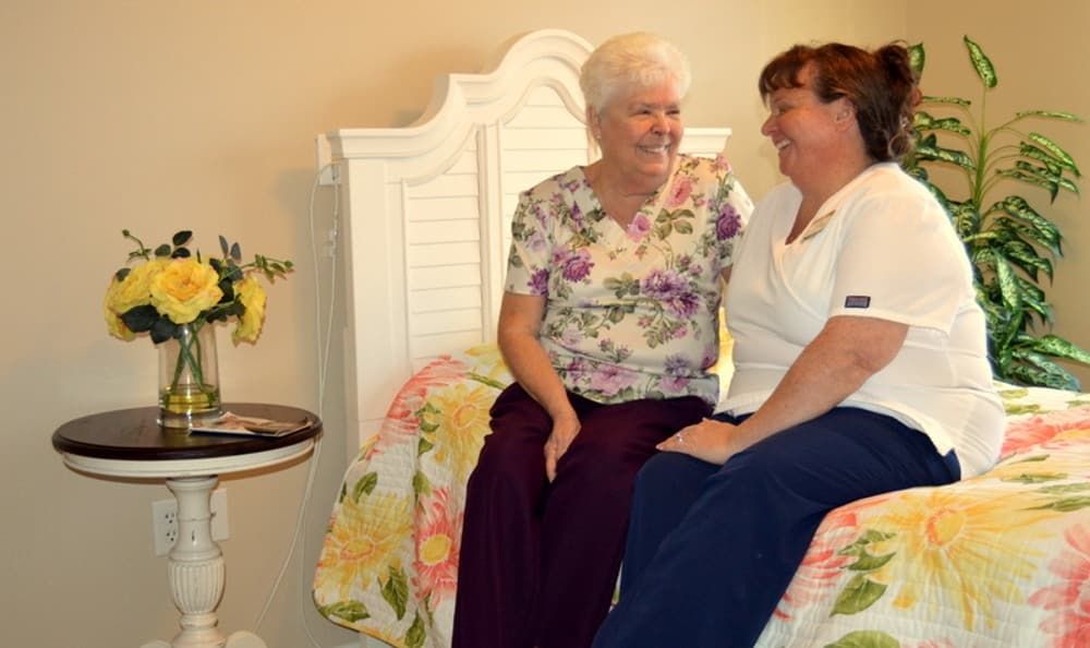 A caregiver and an elderly woman sitting together in a cozy room, sharing a moment of laughter.