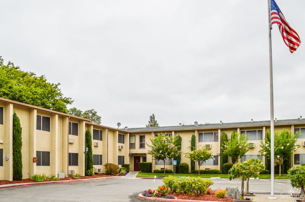 A residential apartment building with well-maintained landscaping under a cloudy sky.