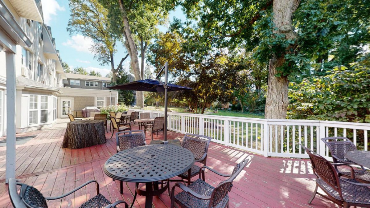 A cozy outdoor patio with tables, chairs, and umbrellas surrounded by lush trees.