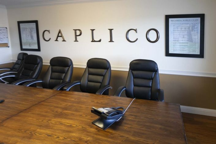 A conference room with a long table, several chairs, and a phone, featuring the Caplico logo on the wall.