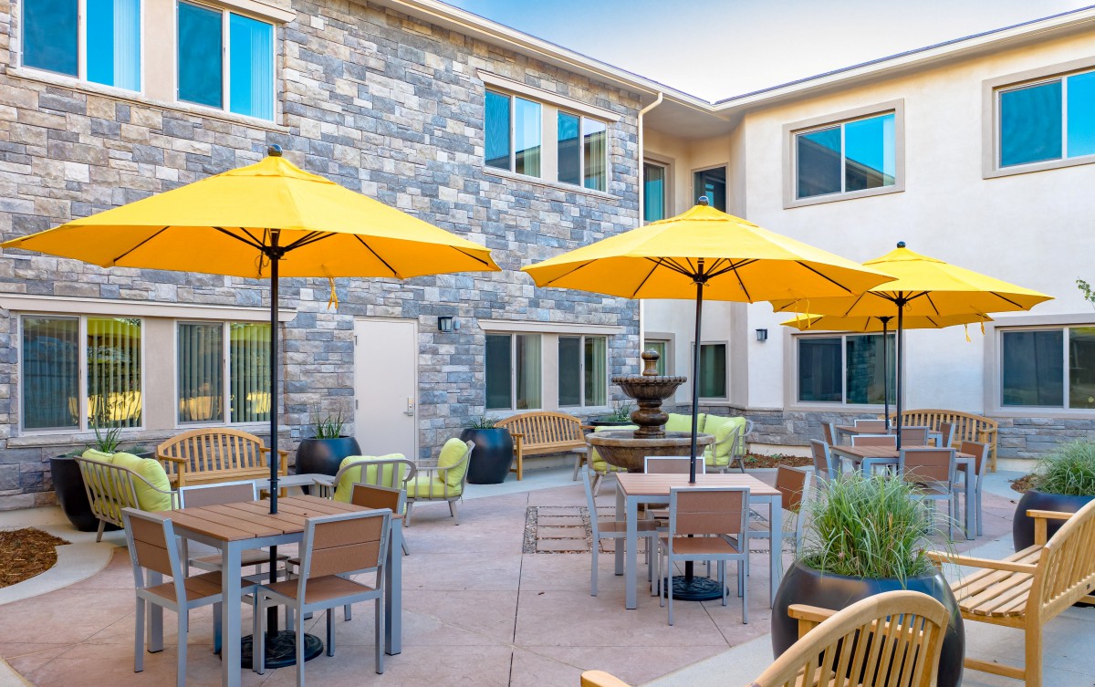 A vibrant courtyard with yellow umbrellas over tables and chairs, set against a stone building.