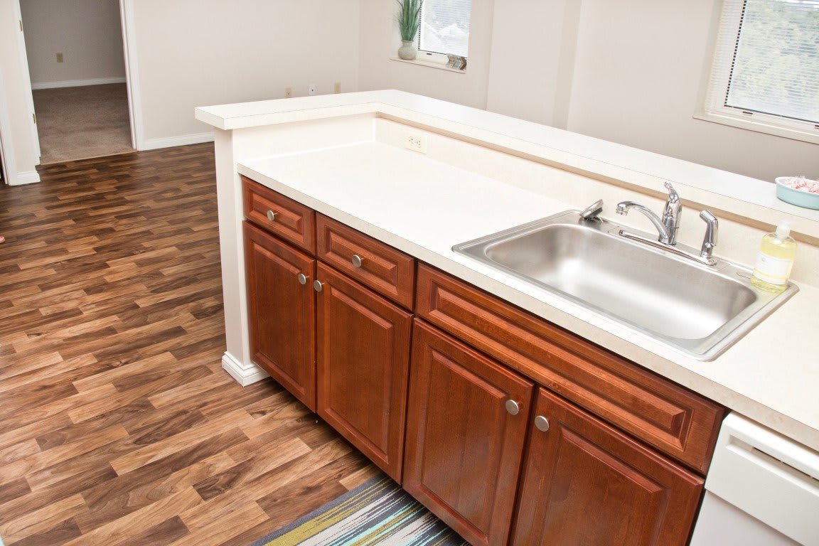 A kitchen with a wooden cabinet and a countertop featuring a sink, set against wood flooring.