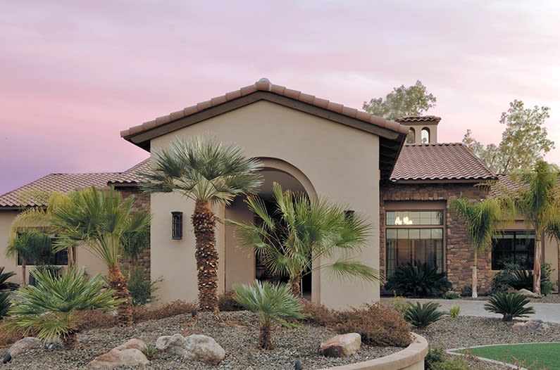 A beautiful house with a desert-style garden and palm trees, set against a sunset sky.