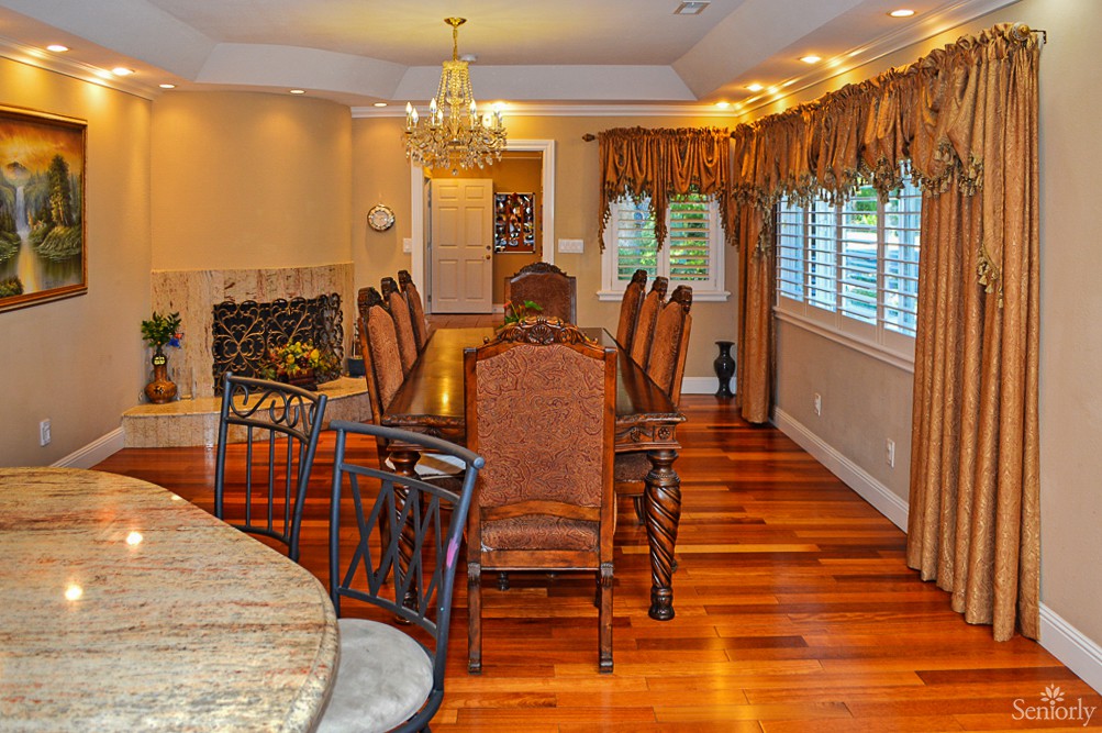 A spacious dining room with a long table, elegant chairs, and a chandelier hanging from the ceiling.