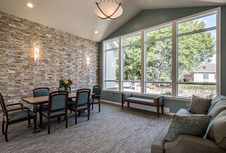 A modern living and dining area featuring a stone accent wall, large windows, and elegant furniture.