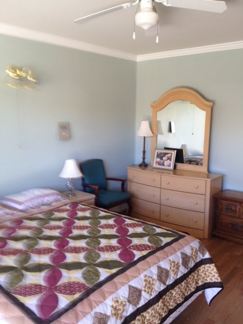 A cozy bedroom featuring a bed with a patterned quilt, a wooden dresser with a mirror, and two lamps.
