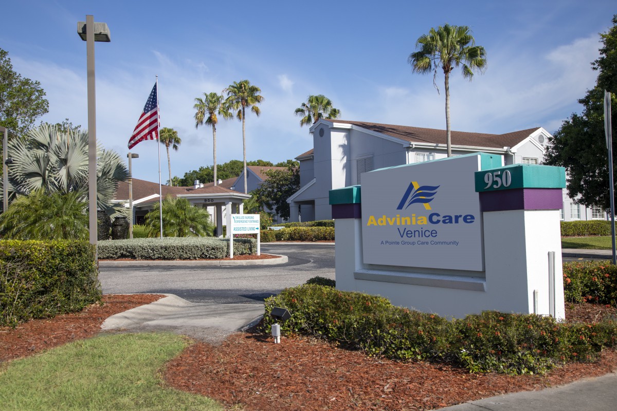 Exterior view of a building with a prominent sign, surrounded by palm trees and an American flag.