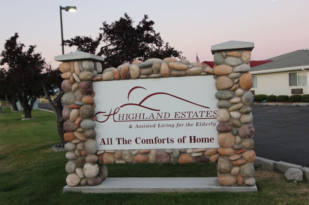 A sign for Highland Estates, a residence for seniors, stands outdoors flanked by stone pillars.