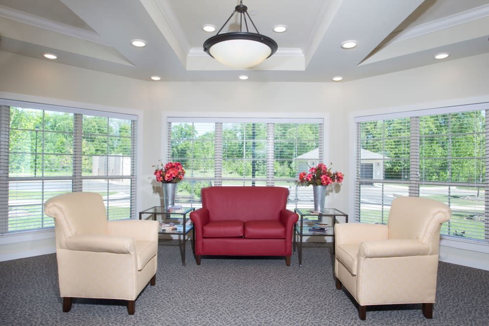A modern living room featuring a central red sofa, beige armchairs, and large windows that allow natural light to fill the space.