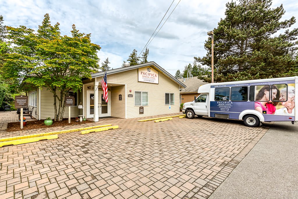 A small building with a van parked outside on a paved driveway, surrounded by trees and an American flag at the entrance.