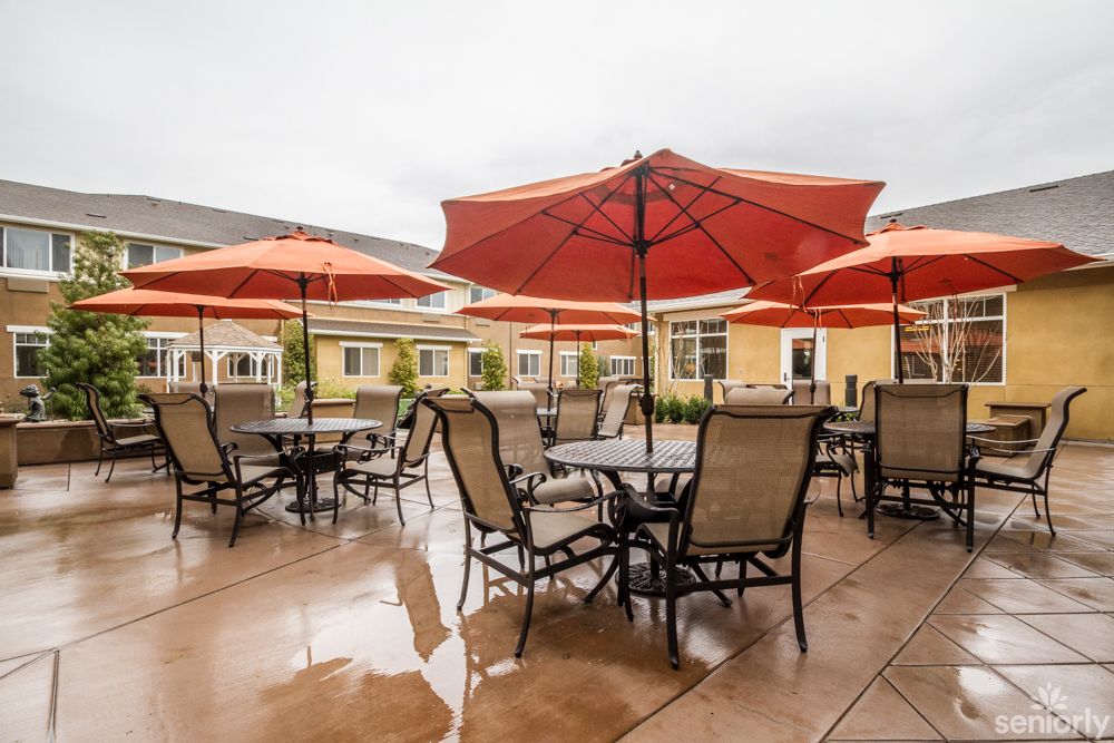 An outdoor patio area with tables, chairs, and red umbrellas on a cloudy day.