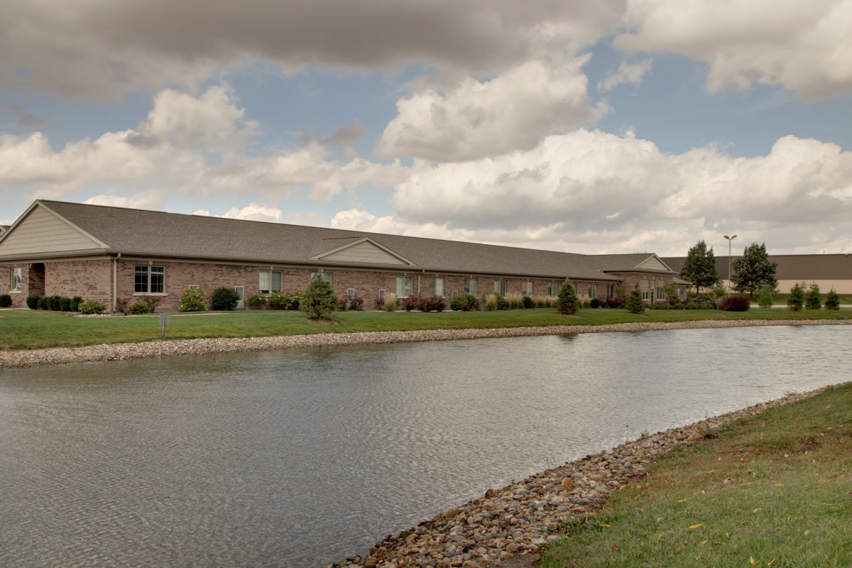 A wide landscape view of a building by a pond under a cloudy sky.
