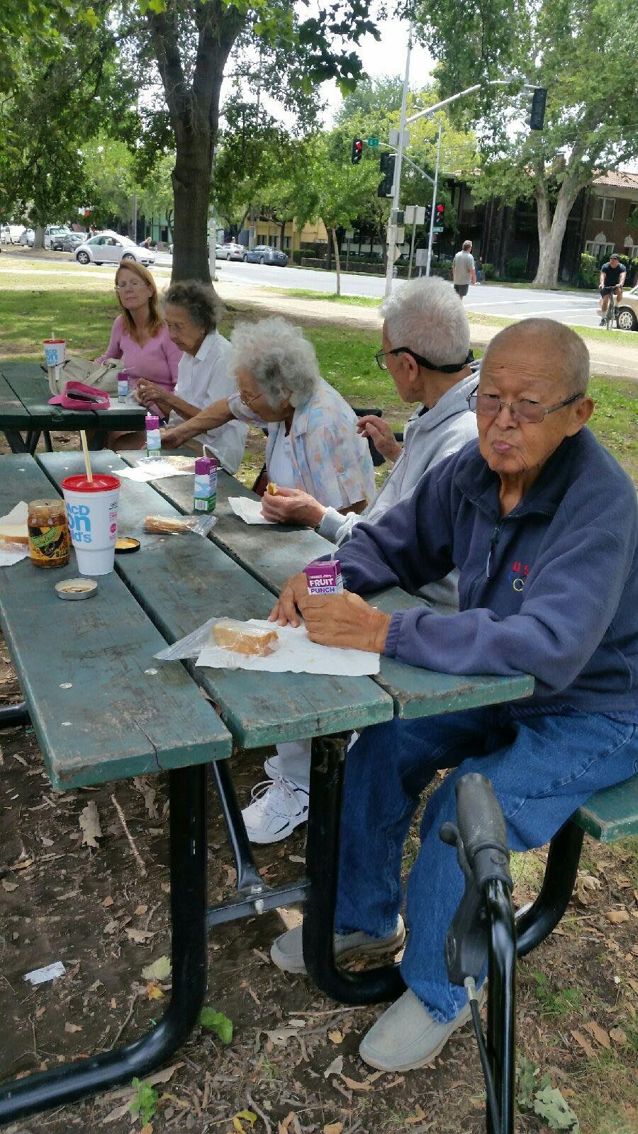 A group of elderly individuals enjoying a picnic at a park table.