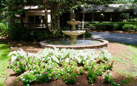 A serene garden with a central fountain surrounded by lush greenery and blooming flowers.