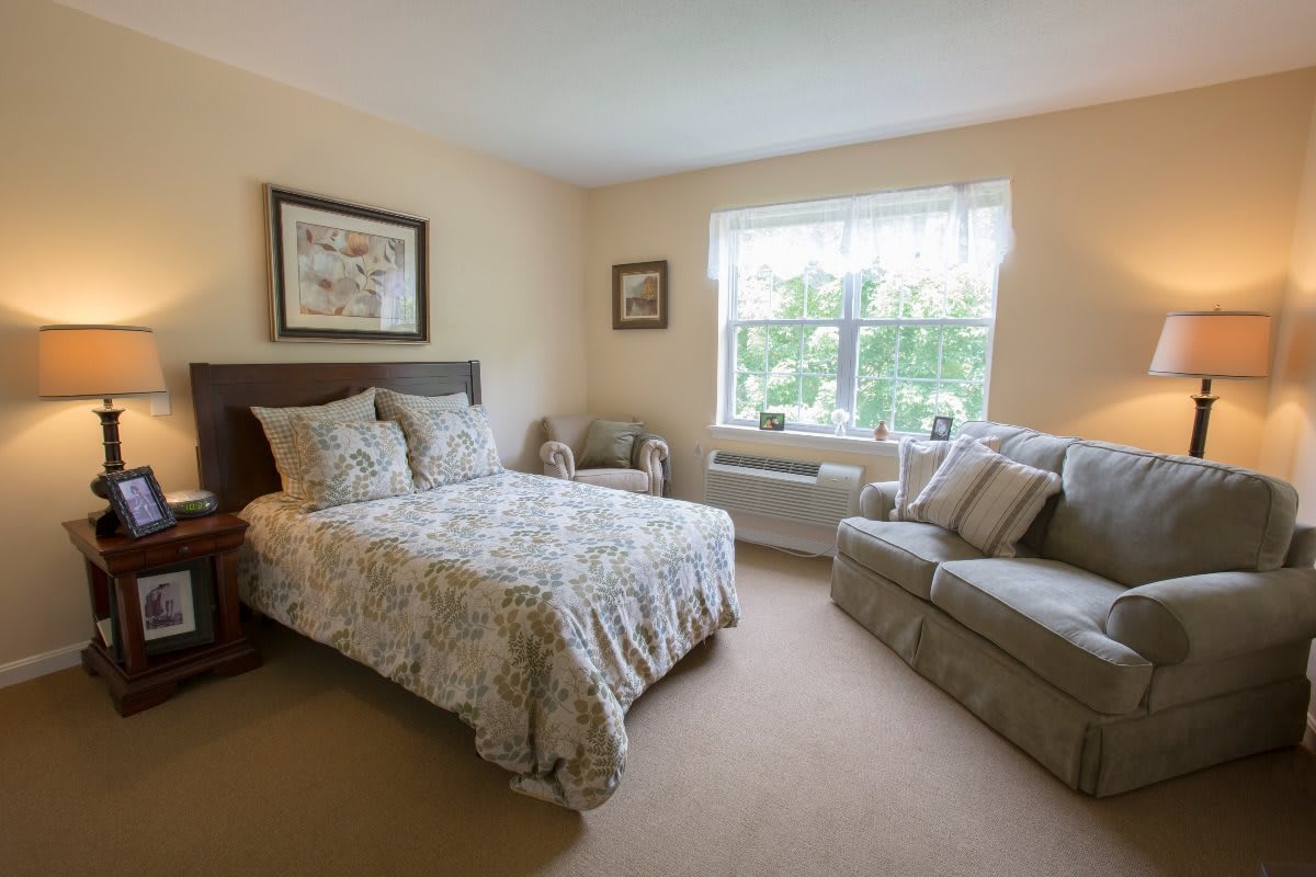 A cozy bedroom with a double bed, sofa, and large window letting in natural light.