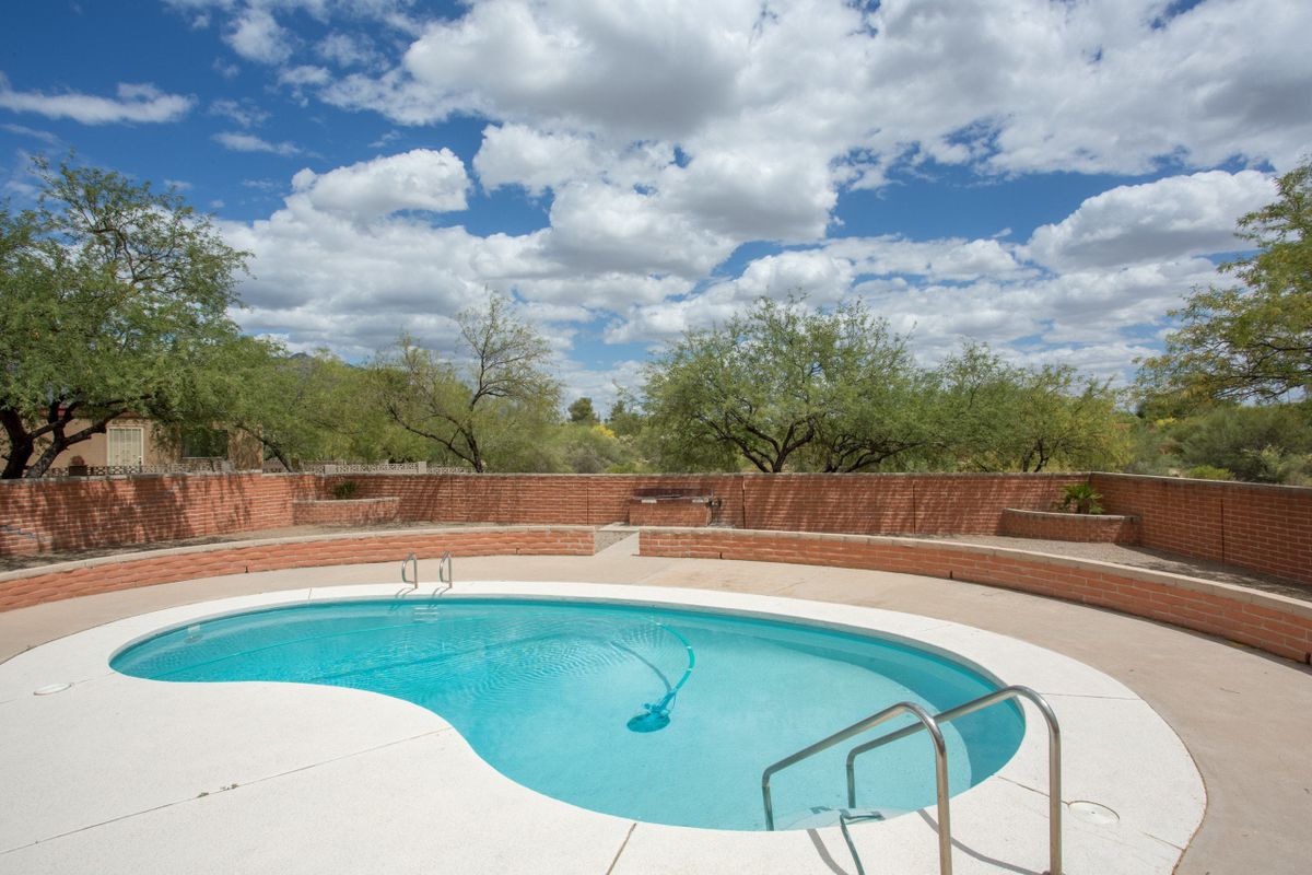 A serene outdoor swimming pool surrounded by desert landscape under a partly cloudy sky.