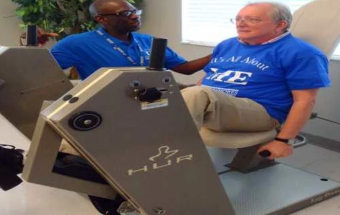 A healthcare worker assists an elderly person using exercise equipment for rehabilitation.